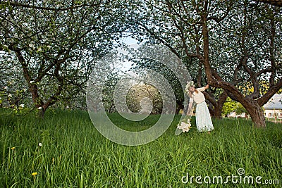 Young beautiful blonde woman in a dress in blooming apple garden - outdoors Stock Photo