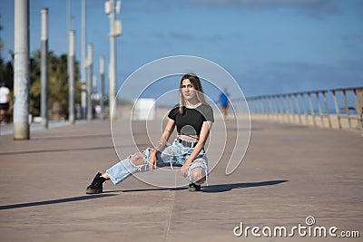 Young, beautiful blonde woman, green eyes, with black top, torn jeans and tattoos, bent over, looking at the camera, rebellious Stock Photo