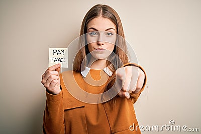 Young beautiful blonde woman holding pay taxes to goverment reminder over yellow background pointing with finger to the camera and Stock Photo