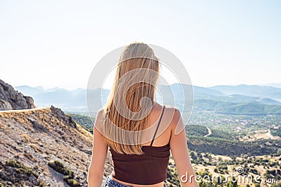Young beautiful blonde woman looks at the horizon. The traveler stands in the mountains Stock Photo