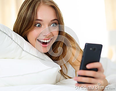 Young beautiful blonde woman lying in bed and holding cellphone Stock Photo