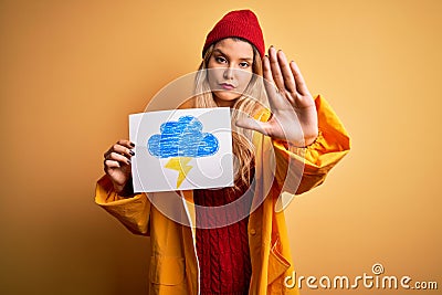 Young beautiful blonde woman wearing raincoat holding banner with cloud thunder image with open hand doing stop sign with serious Stock Photo