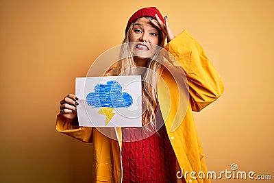 Young beautiful blonde woman wearing raincoat holding banner with cloud thunder image stressed with hand on head, shocked with Stock Photo