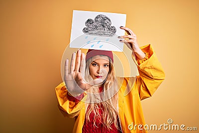 Young beautiful blonde woman wearing raincoat and wool cap holding banner with cloud image with open hand doing stop sign with Stock Photo