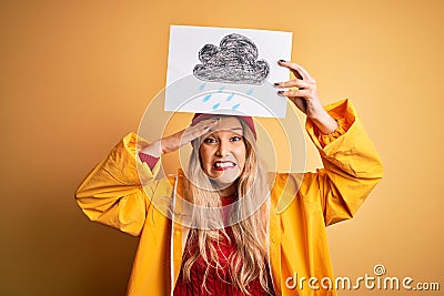 Young beautiful blonde woman wearing raincoat and wool cap holding banner with cloud image stressed with hand on head, shocked Stock Photo