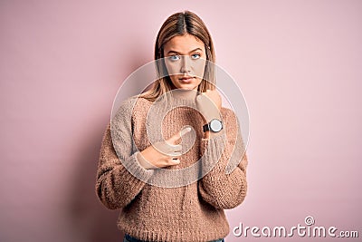 Young beautiful blonde woman wearing winter wool sweater over pink isolated background In hurry pointing to watch time, Stock Photo