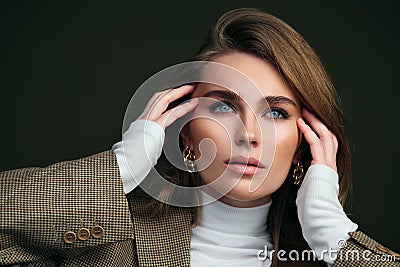 A young beautiful blonde woman in a white turtleneck and a man`s jacket poses on a green olive background in the studio. Stock Photo