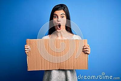 Young beautiful brunette activist woman holding blank cardboard banner protesting scared in shock with a surprise face, afraid and Stock Photo