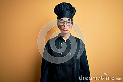 Young beautiful brunette chef woman wearing cooker uniform and hat over yellow background depressed and worry for distress, crying Stock Photo