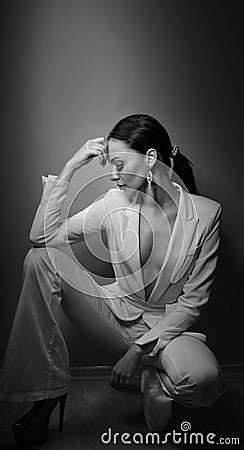 Young beautiful brunette woman in elegant white suit with trousers sitting. Seductive dark hair girl posing, studio shot. Elegant Stock Photo