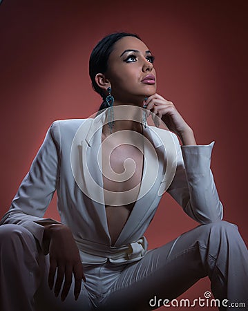 Young beautiful brunette woman in elegant white suit with trousers sitting. Seductive dark hair girl posing, studio shot. Elegant Stock Photo