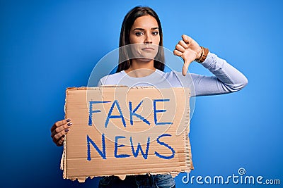 Young beautiful brunette woman holding banner with fake news message with angry face, negative sign showing dislike with thumbs Stock Photo