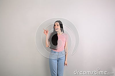 Young beautiful brunette woman with long hair standing by the grey background wearing jeans and pink shirt surprised Stock Photo