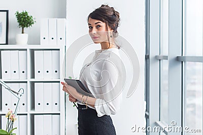 Young beautiful businesswoman using tablet with internet in office, reading and sending messages, smiling, looking at Stock Photo