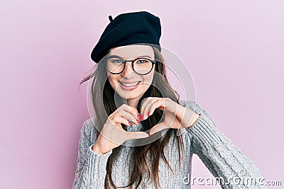 Young beautiful caucasian girl wearing french look with beret smiling in love doing heart symbol shape with hands Stock Photo