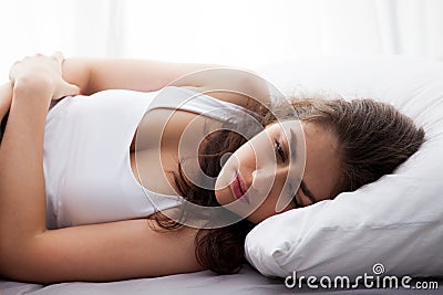 Young beautiful Caucasian woman on bed being sad, depressed, having stomach pain, having food poisoning, cramps sickness Stock Photo