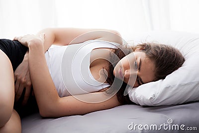 Young beautiful Caucasian woman on bed being sad, depressed, having stomach pain, having food poisoning, cramps sickness. Stock Photo