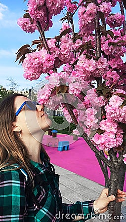 Young beautiful caucasian woman in profile in sunglasses sniffing pink sakura flowers. Spring blossom Stock Photo