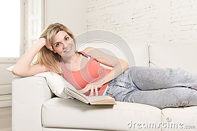 Young beautiful caucasian woman reading book studying lying comfortable on home sofa looking happy Stock Photo