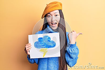 Young beautiful chinese woman holdig cloud and thunder draw pointing thumb up to the side smiling happy with open mouth Stock Photo