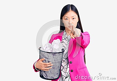 Young beautiful chinese woman holding paper bin full of crumpled papers pointing with finger to the camera and to you, confident Editorial Stock Photo
