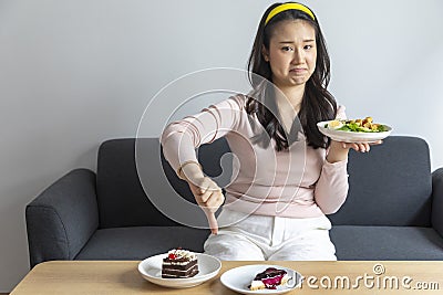 Young beautiful Chinese woman prefer eating salad and using hand push out, deny chocolate cake or dessert. Stock Photo