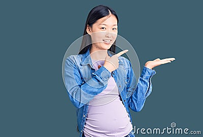Young beautiful chinese woman pregnant expecting baby amazed and smiling to the camera while presenting with hand and pointing Editorial Stock Photo