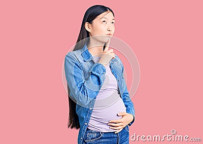 Young beautiful chinese woman pregnant expecting baby thinking concentrated about doubt with finger on chin and looking up Stock Photo