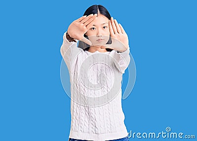 Young beautiful chinese woman wearing casual sweater doing frame using hands palms and fingers, camera perspective Editorial Stock Photo