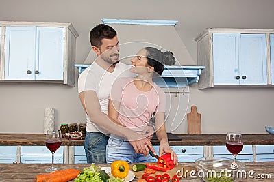 Young beautiful couple hugging in the kitchen cooking together a salad. They smile at each other Stock Photo