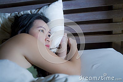 Young beautiful depressed and sad Asian Chinese woman having insomnia lying in bed at night sleepless suffering anxiety stress and Stock Photo