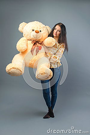 Young beautiful girl with big teddy bear soft toy happy smiling and playing on grey background Stock Photo