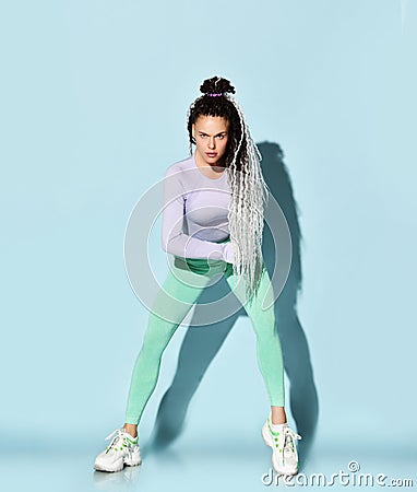 Young beautiful girl with blond dreadlocks hairstyle in sexy sportswear and sneakers stretching on floor working on body balance Stock Photo