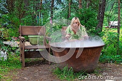A young beautiful girl, a blonde witch is preparing a potion in a large cauldron on the eve of Halloween or the worshiping devil Stock Photo