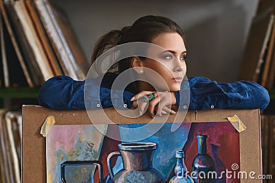 Young beautiful girl, female artist painter thinking of a new artwork idea or project holding a finished picture artwork Stock Photo