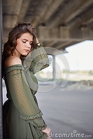 A young beautiful girl in a green dress poses under a concrete bridge, modern architecture Stock Photo