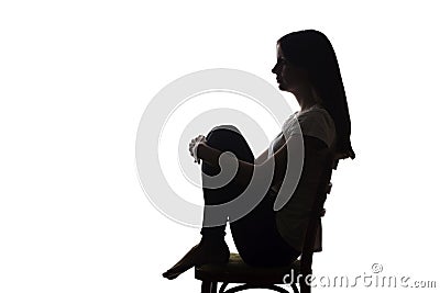 Young beautiful girl in grief hugged her knees - silhouette Stock Photo