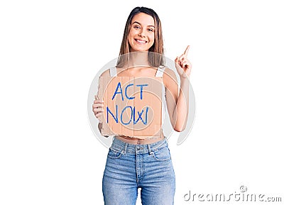 Young beautiful girl holding act now banner surprised with an idea or question pointing finger with happy face, number one Stock Photo