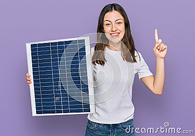 Young beautiful girl holding photovoltaic solar panel surprised with an idea or question pointing finger with happy face, number Stock Photo