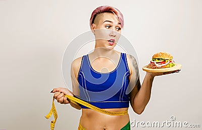 Young beautiful girl holds hamburger and measuring tape, on a light background Stock Photo