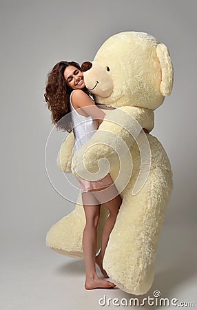 Young beautiful girl hugging big teddy bear soft toy happy smiling Stock Photo