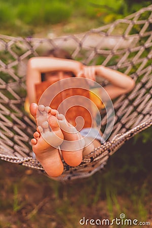 A young beautiful girl lies in a hammock. Rest, summer vacation, leisure time concept. Selective focus on feets. Vertical image Stock Photo