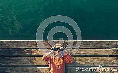 Young Beautiful Girl Lies On A Pier Near The Sea And Looks Through Binoculars On The Sky. Travel Search Journey Concept Stock Photo