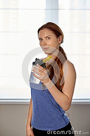 A young beautiful girl, stands at the window with a shaker in her hands. Stock Photo