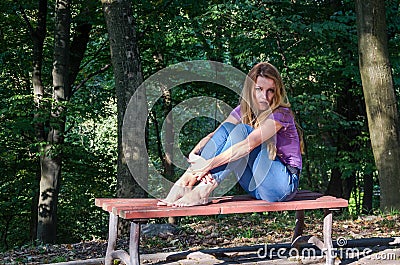 Young beautiful girl model in jeans and a T-shirt with long blond hair and sad smiles pensively posing for a walk in the autumn pa Stock Photo