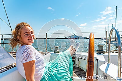 Young beautiful girl sits on a yacht near the helm in the sea and looks at the camera on the deck. Stock Photo
