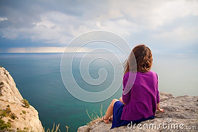 Beautiful girl sitting on rock and looking at sea Stock Photo