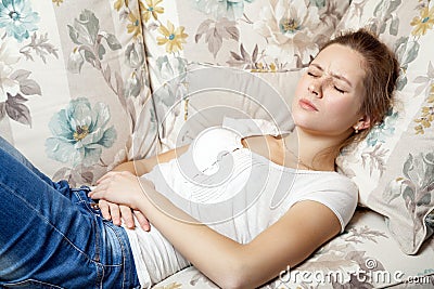 Young beautiful girl with stomach pain lying on the sofa. Stock Photo