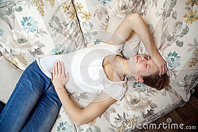 Young beautiful girl with stomach pain lying on the sofa. Stock Photo