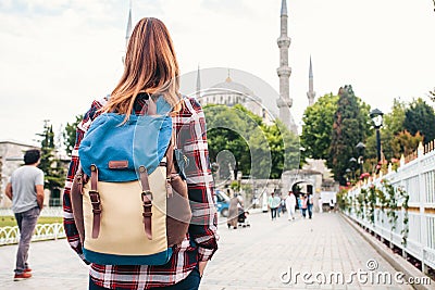 Young beautiful girl traveler with a backpack looking at a blue mosque - a famous tourist attraction of Istanbul. Travel Stock Photo